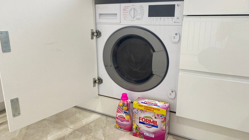 Built-in washing machine with cleaning products and supplies on floor below