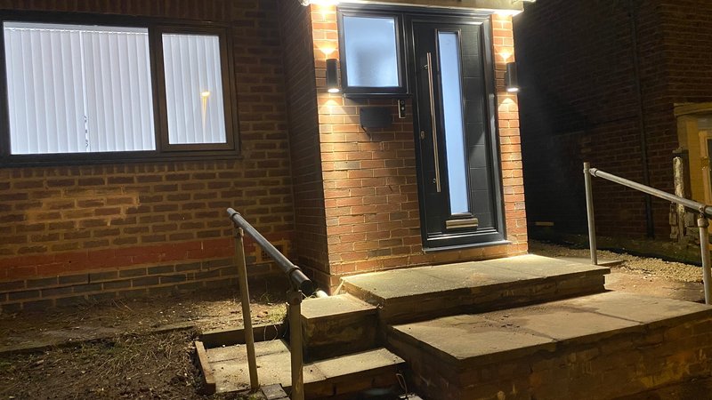 Brick building exterior with illuminated entrance door, steps, and metal handrails at night