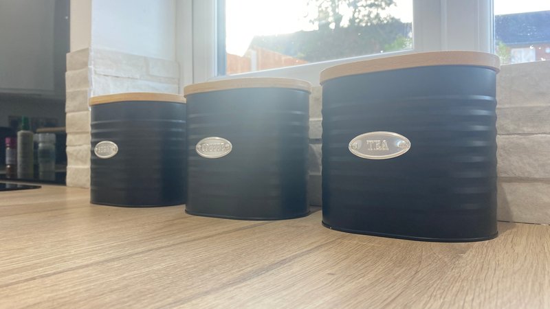 Three black cylindrical storage containers with wooden lids on kitchen worktop