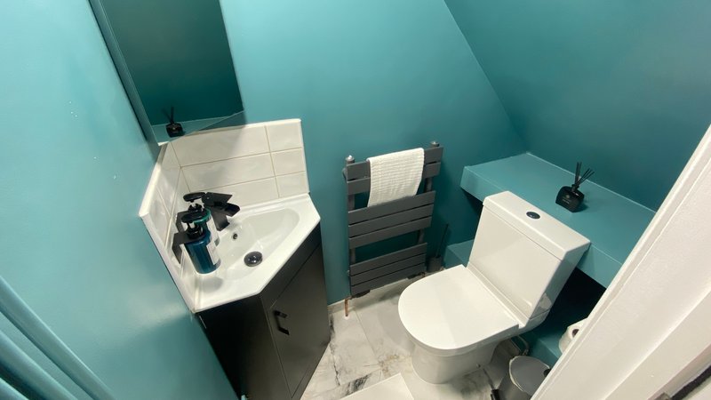 Compact bathroom with curved sink, heated towel rail, toilet and turquoise walls