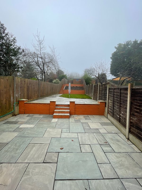 Garden patio with stone paving, wooden raised beds, and fencing, lawn beyond