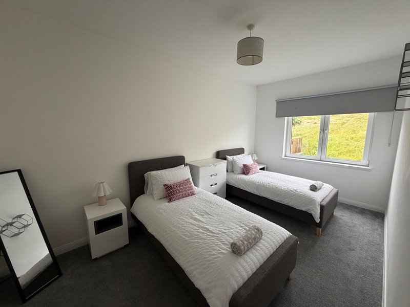 Twin bedroom with two single beds, white bedside tables, pendant light, and window with garden view