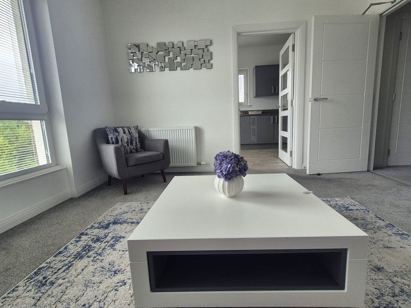 Modern living room with white coffee table, dark armchair, purple flowers, and geometric wall art