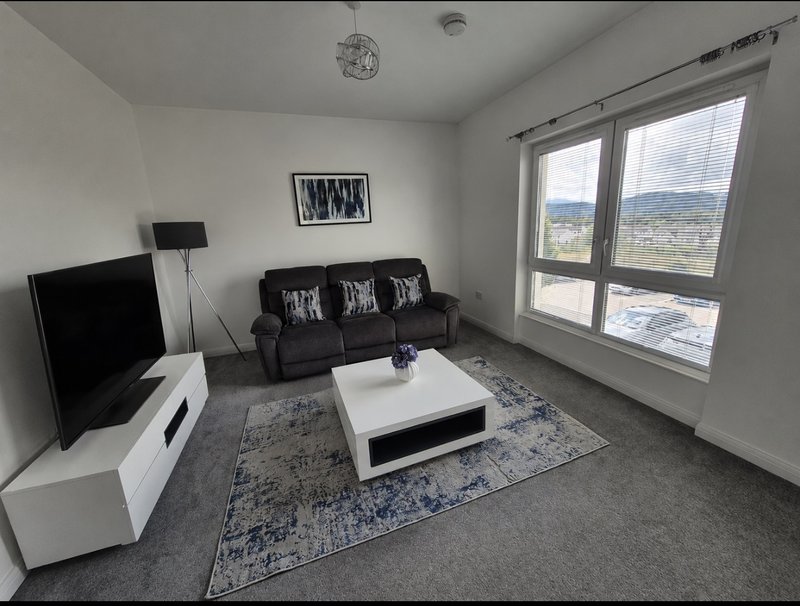 Modern living room with dark sofa, white coffee table, TV, and large windows overlooking countryside