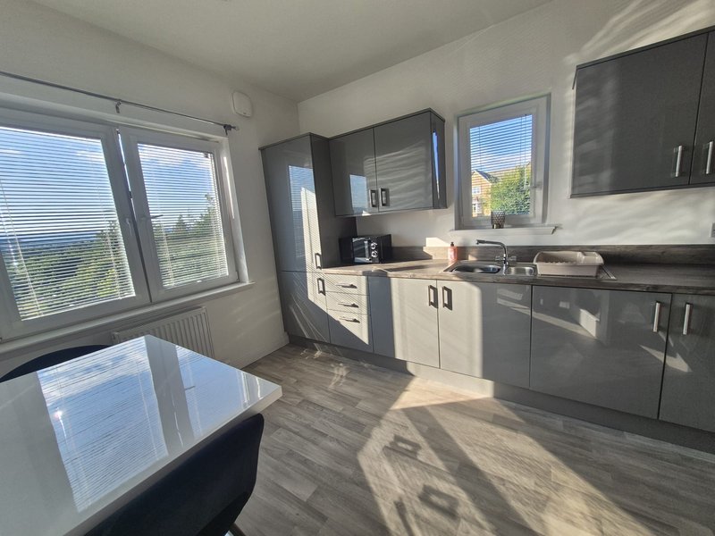 Modern kitchen with dark grey units, white worktops, dining table and large windows with rural views
