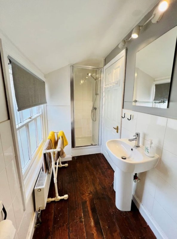 Modern bathroom with shower enclosure, pedestal sink, dark wood flooring and heated towel rail