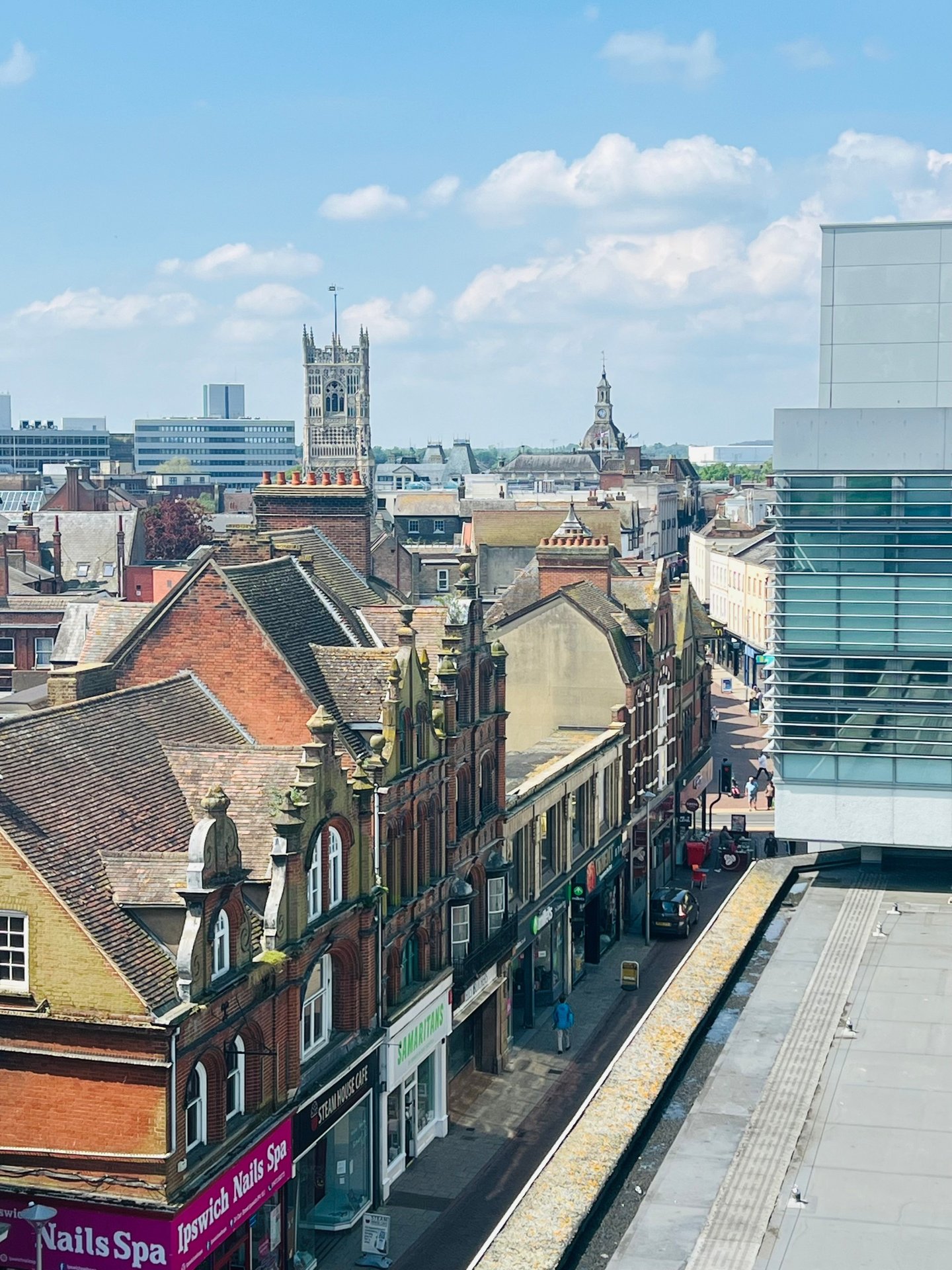 Urban street view from above showing historic buildings, shops, and city skyline with church spire