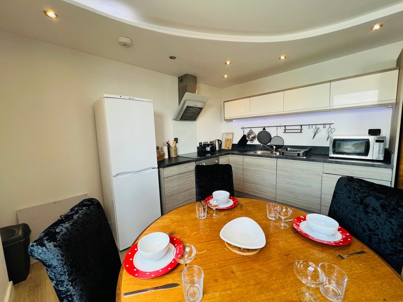 Modern kitchen and dining area with white cabinetry, round wooden table set for dining, and black upholstered chairs
