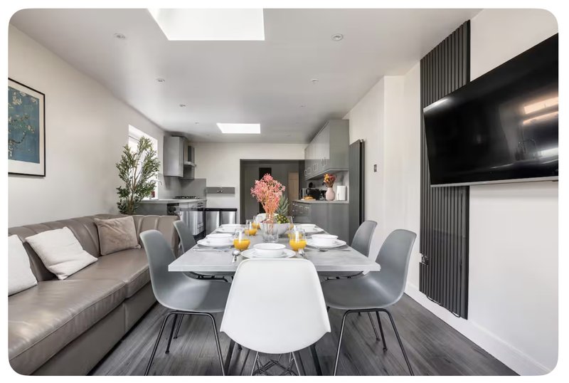 Modern open-plan living and dining area with sofa, dining table, chairs, and wall-mounted TV