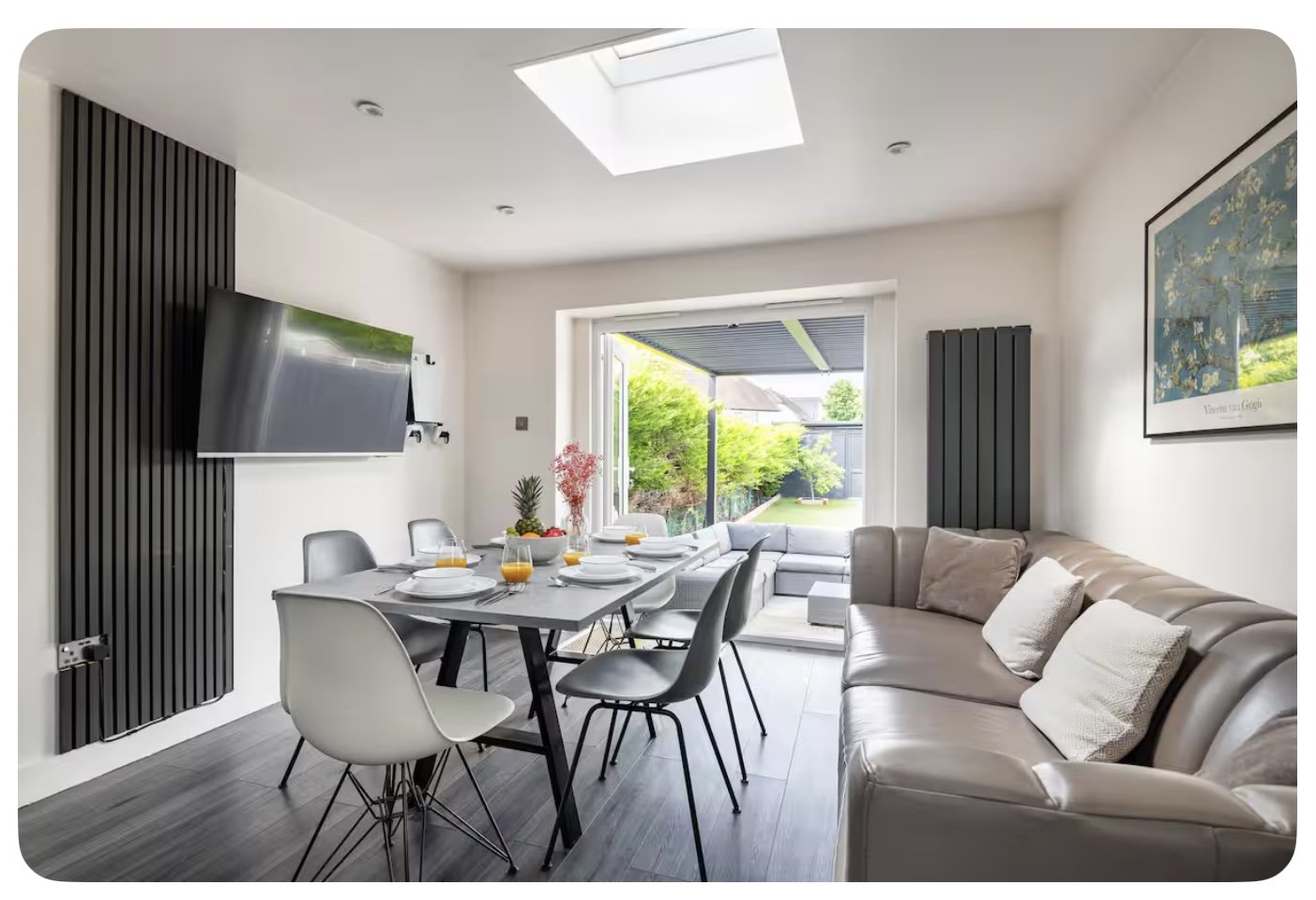 Modern open-plan living area with dining table, chairs, grey sofa and garden views through patio doors