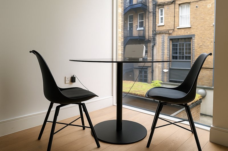 Modern dining area with black chairs, glass table, and street-view window overlooking brick buildings