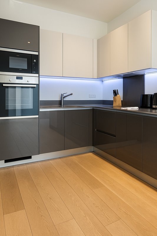 Modern kitchen with cream and dark cabinetry, LED backlighting, wooden flooring and stainless steel appliances