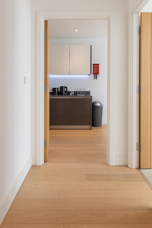 Modern hallway with wood flooring leading to kitchenette with dark cabinetry and appliances