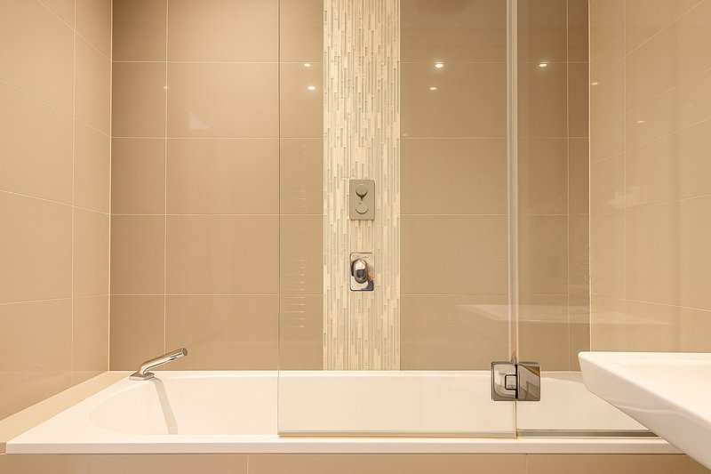Modern bathroom with large white bathtub, beige tile walls and chrome fixtures