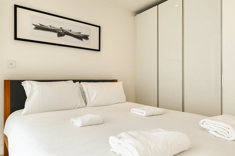 Modern bedroom with double bed, white bedding, wooden headboard and fitted wardrobes