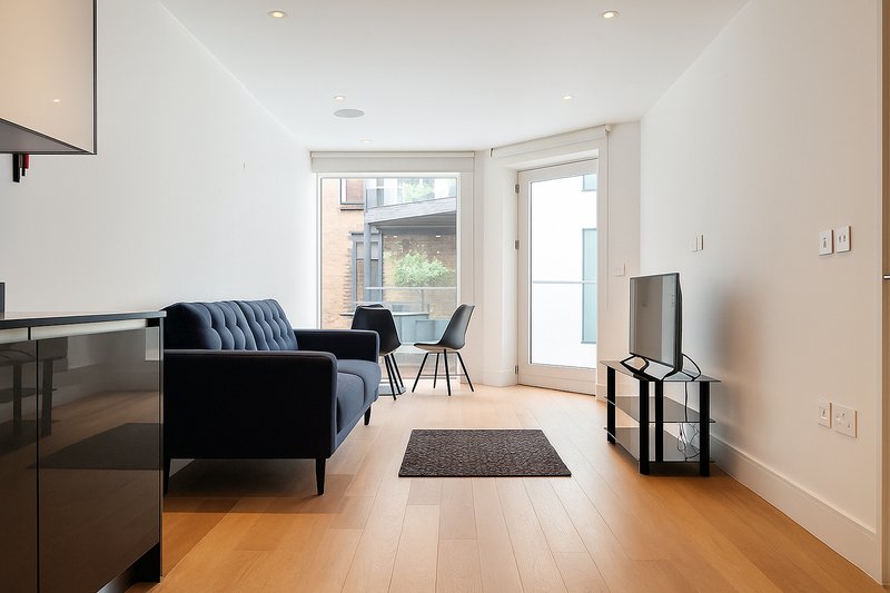 Modern living room with navy sofa, wooden flooring, glass doors and minimalist decor