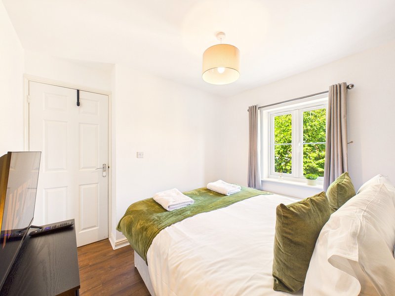 Bright bedroom with double bed, green bedding, white wardrobe and garden view through windows