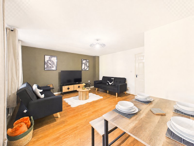 Open-plan living and dining area with black sofas, TV, wooden dining table and hardwood flooring