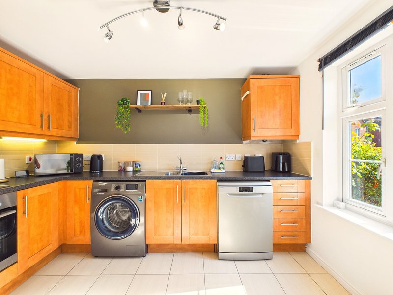 Modern kitchen with orange cabinetry, washing machine, dishwasher, and window with garden view