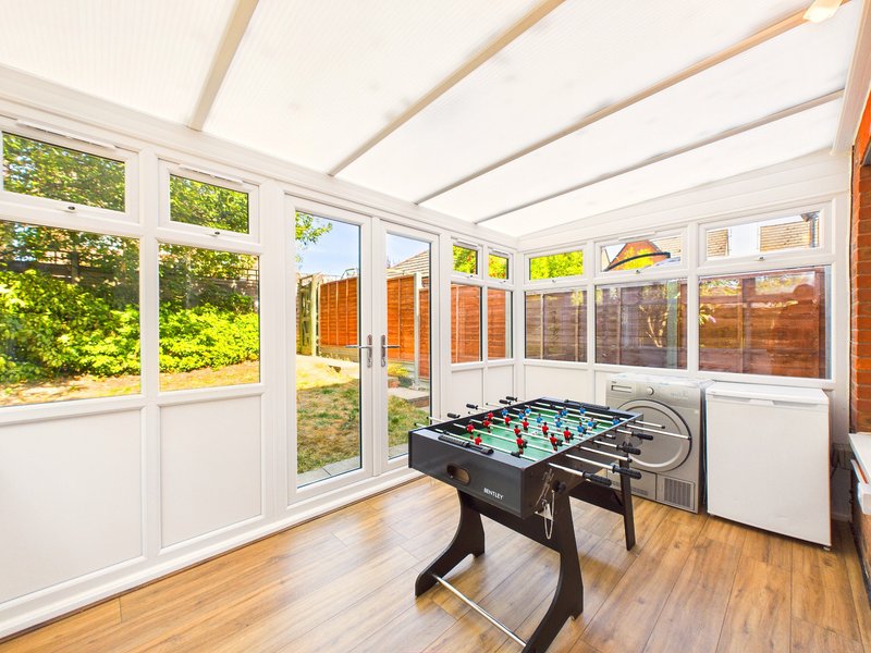 Bright conservatory with foosball table, wooden floor, white walls and glass doors leading to garden