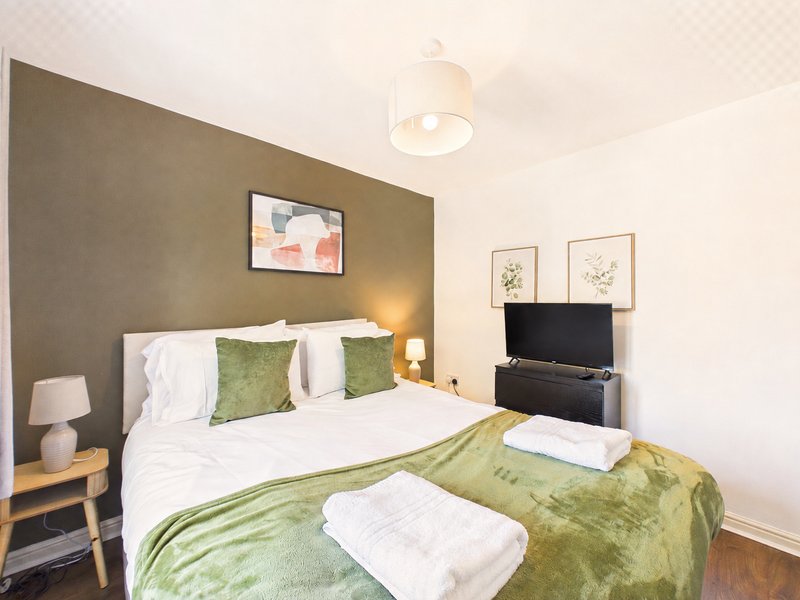 Modern bedroom with double bed, green throw, white pillows and wall-mounted TV
