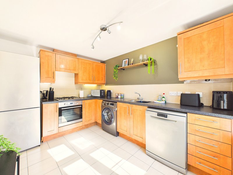 Modern kitchen with orange wooden cabinets, white appliances, black countertop and tiled floor