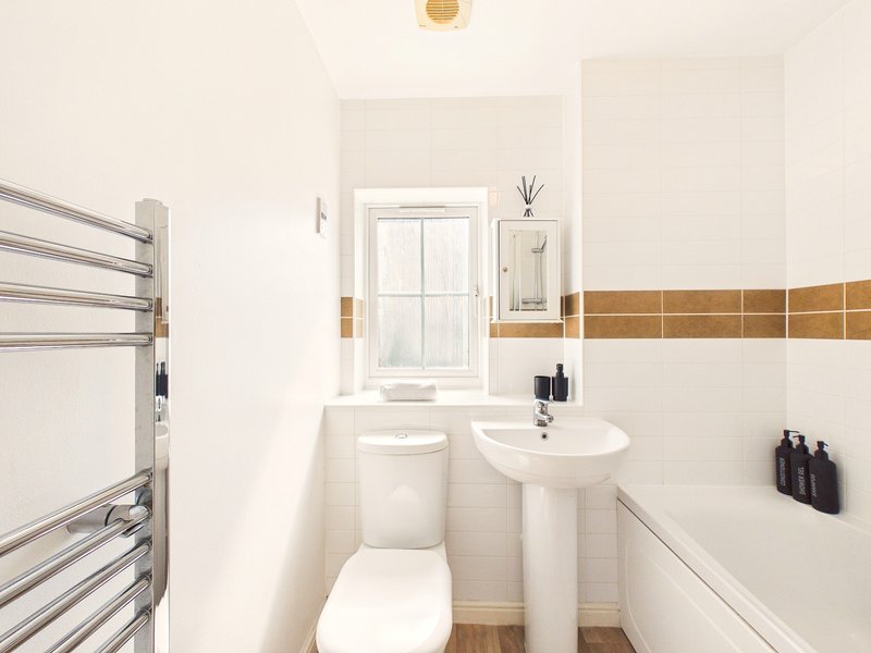 Clean bathroom with pedestal sink, toilet, heated towel rail and window