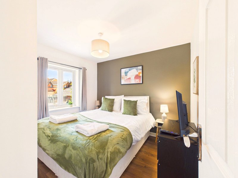 Bright bedroom with double bed, green bedding, accent wall, window and wooden floor