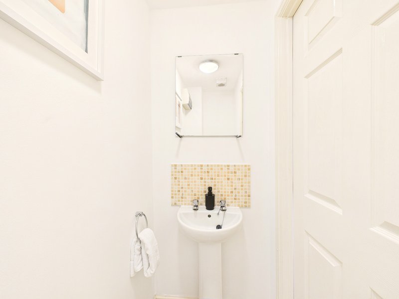 Small bathroom with pedestal sink, wall-mounted mirror, and mosaic tile splashback