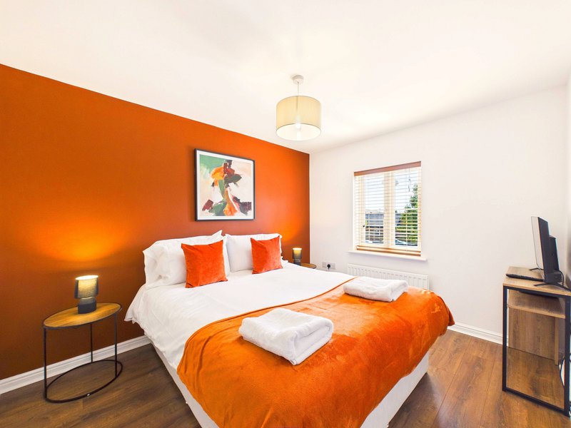 Modern bedroom with orange accent wall, white and orange bedding, wooden floor and pendant light
