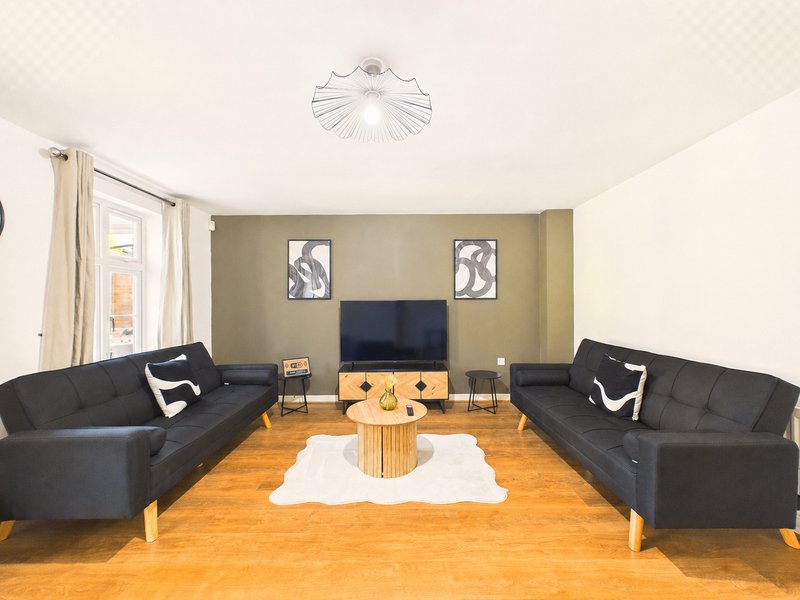 Living room with two black sofas, wooden coffee table, TV, and hardwood flooring