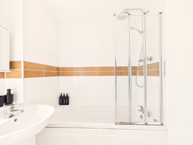 Modern bathroom with white sink, tiled walls, brown accent band, and glass shower enclosure