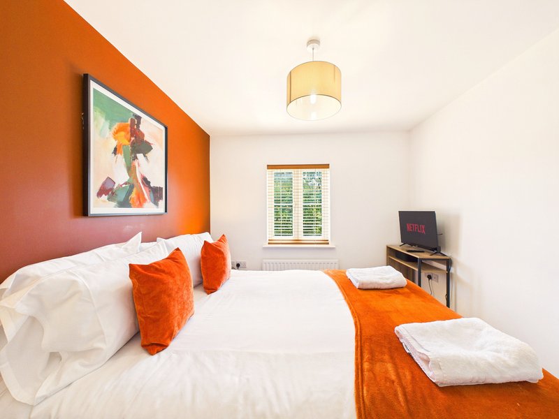 Bright bedroom with double bed, orange accent wall, matching cushions and throw blanket