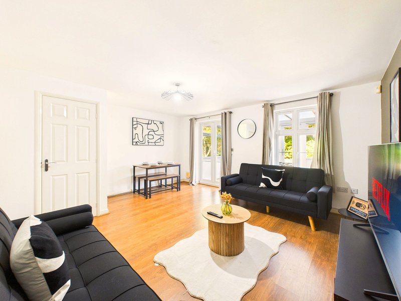 Spacious living room with black sofas, wooden floor, white walls and large windows