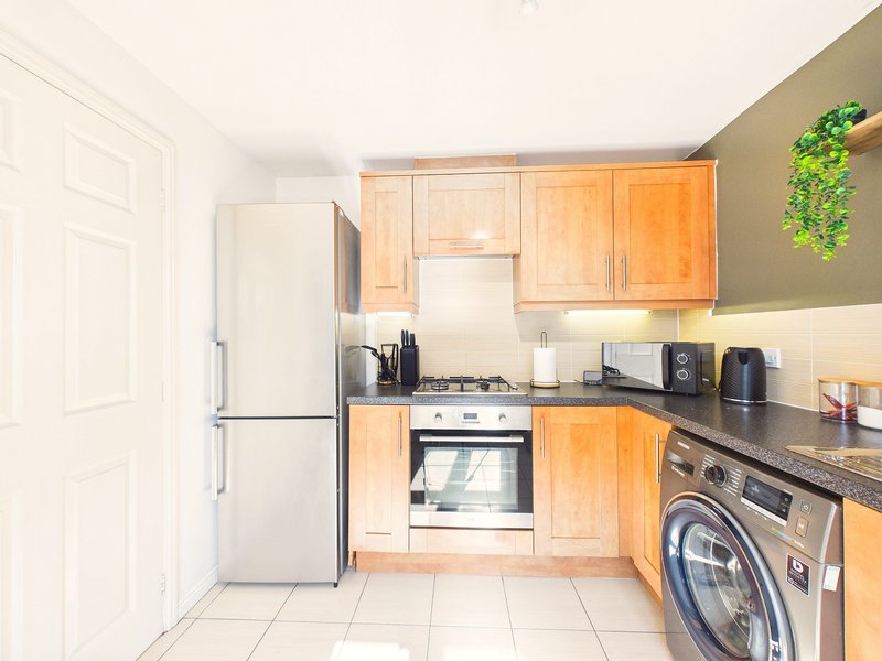 Kitchen with wooden cabinets, white fridge, gas hob, oven, and washing machine