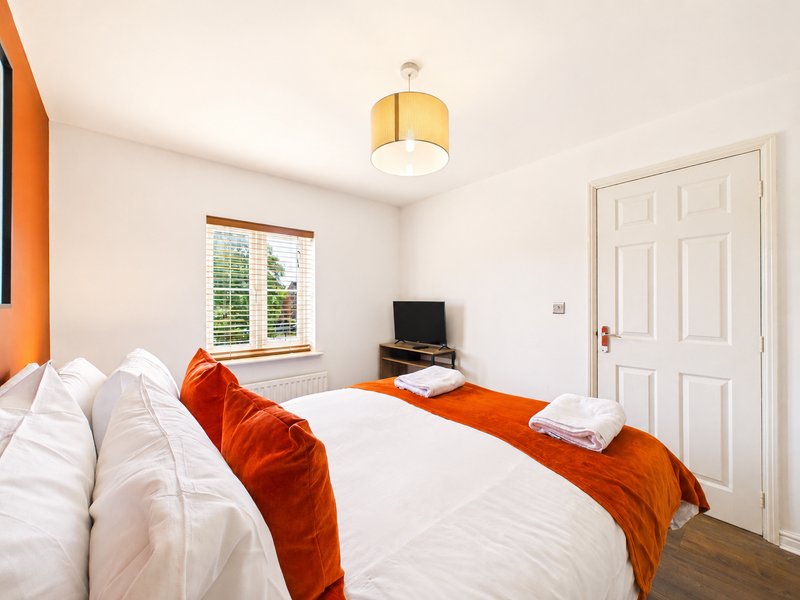 Bright bedroom with double bed, orange velvet throws, white bedding, ceiling lamp and window