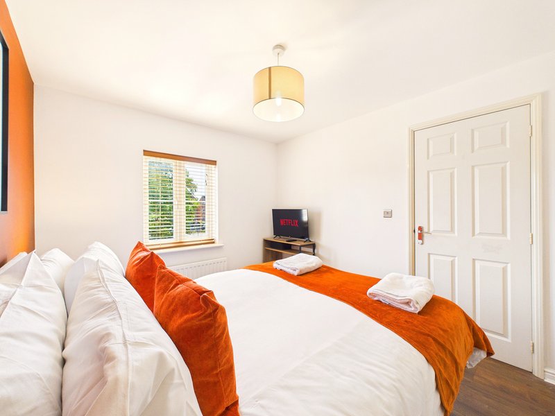 Bright bedroom with double bed, orange throws, white pillows, window and wooden floor