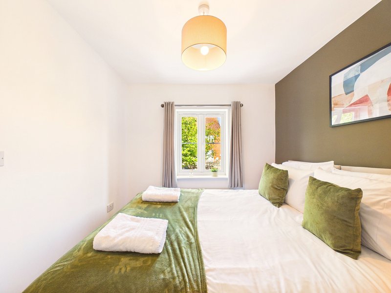 Bright bedroom with double bed, green cushions, pendant light and garden view