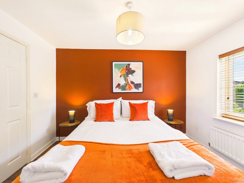 Bedroom with orange accent wall, double bed, white bedding, orange throw, and bedside lamps