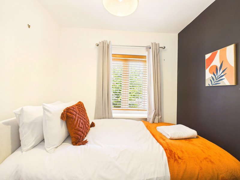 Modern bedroom with double bed, white pillows, orange throw blanket and wall art