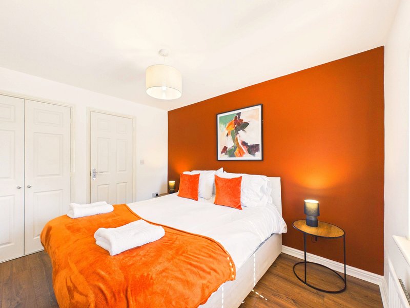 Bedroom with double bed, orange feature wall, white wardrobe doors and wooden flooring