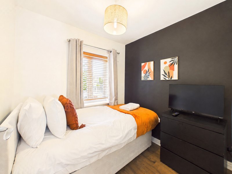 Modern bedroom with white bed, orange throw, dark accent wall, TV and window