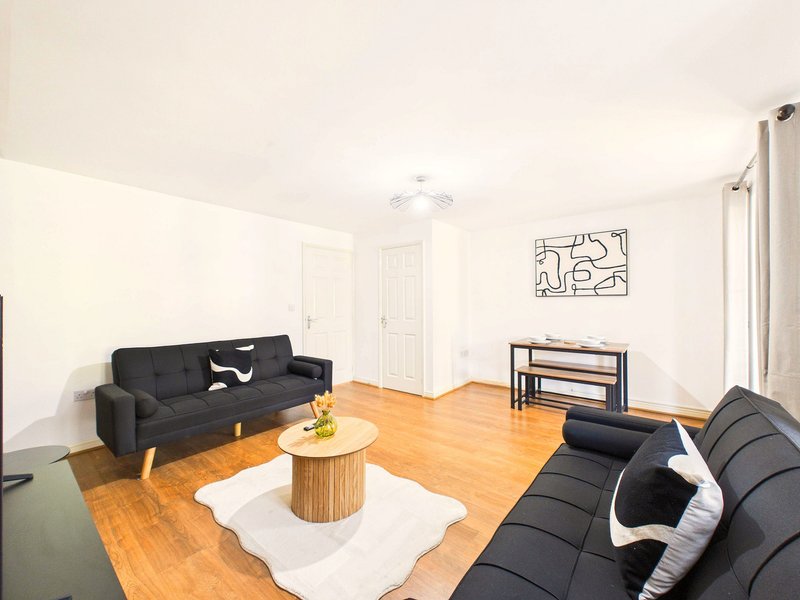 Bright living room with black sofas, wooden floor, coffee table and wall art