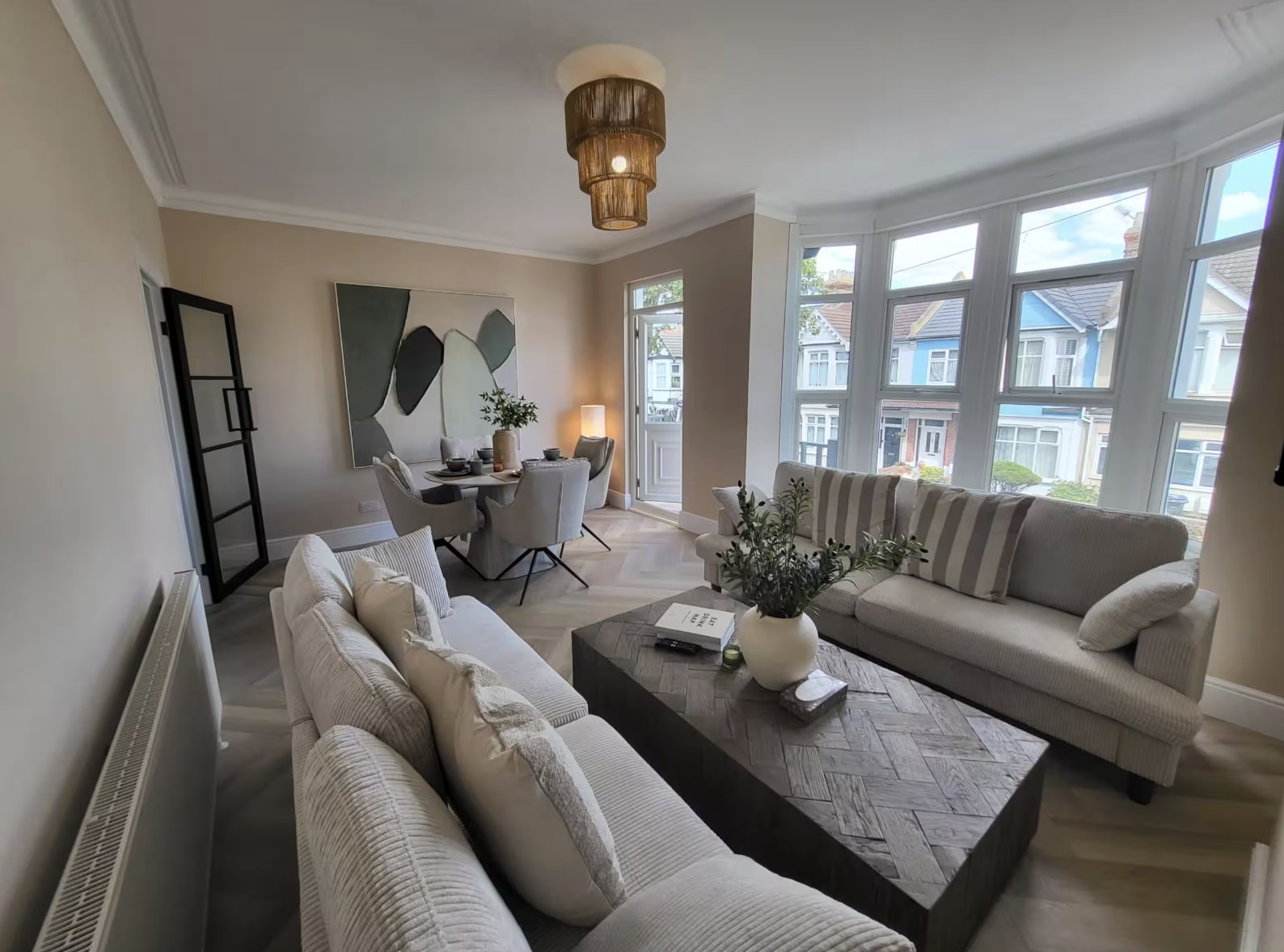 Bright living room with cream sofas, dark coffee table, and large bay windows overlooking street
