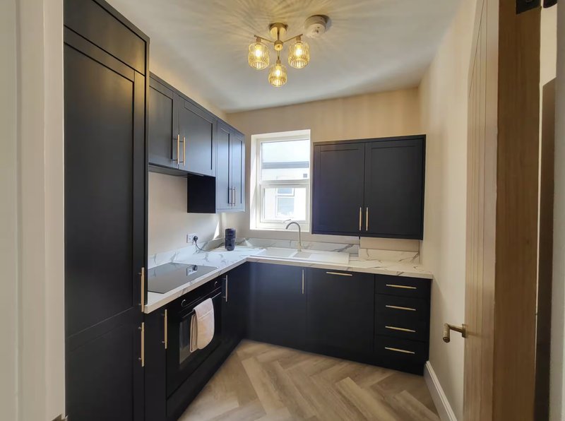 Modern kitchen with black cabinetry, white countertops, integrated appliances and pendant lighting