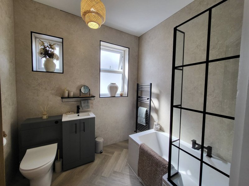 Modern bathroom with black vanity, toilet, bathtub, glass shower enclosure and window