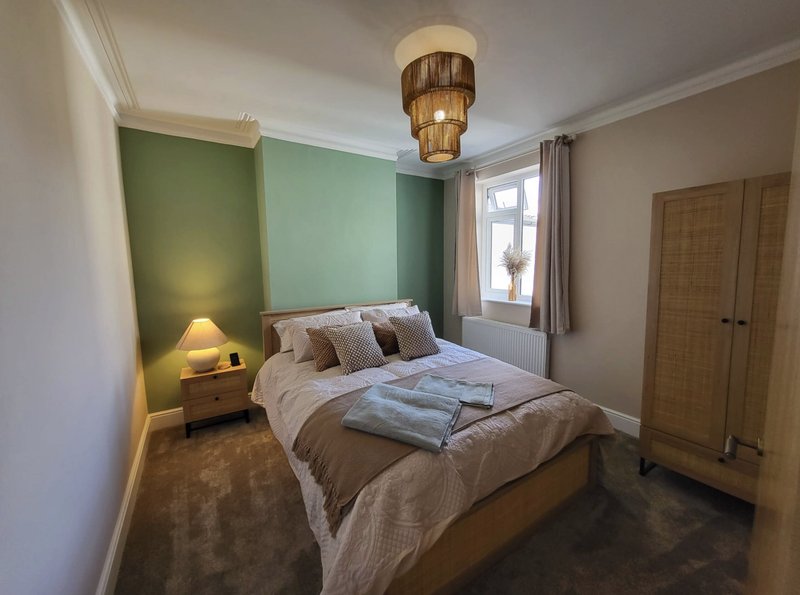 Bedroom with double bed, green accent wall, bedside lamp, wooden wardrobe and pendant light