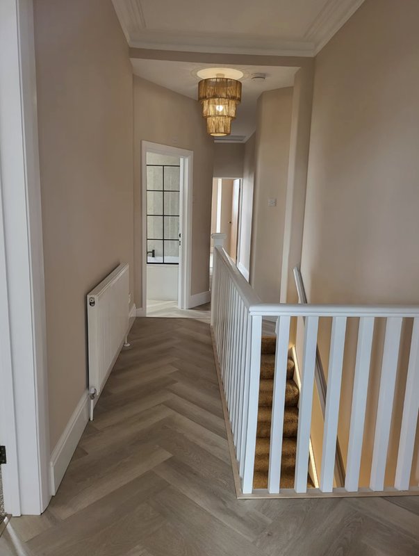 Hallway with herringbone wood flooring, white stair railing, and ceiling pendant light