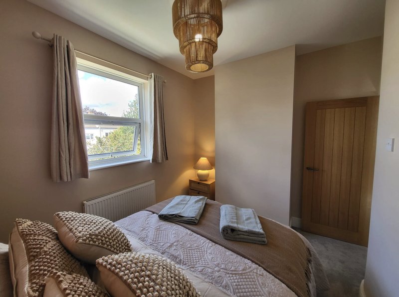 Bedroom with double bed, woven pendant light, window with curtains, and wooden door