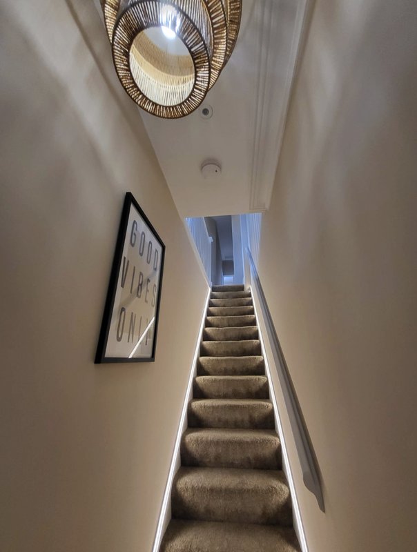 Staircase with rattan ceiling light, framed artwork on wall, and natural light from above